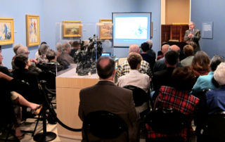 a seated audience at a lecture in museum gallery