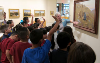 woman pointing to painting in front of group of students