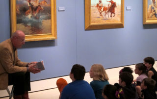 man reading to group of students in front of a painting