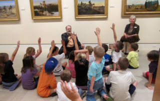 seated man pointing to group of children with raised hands