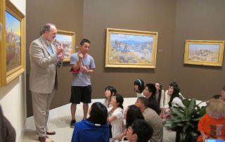 two adults signing to a group of teens seated on floor of museum gallery