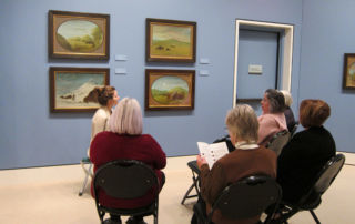 group of adults seated around and looking at painting in museum gallery