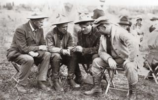 a group of four seated men looking at something in the hands of the middle man