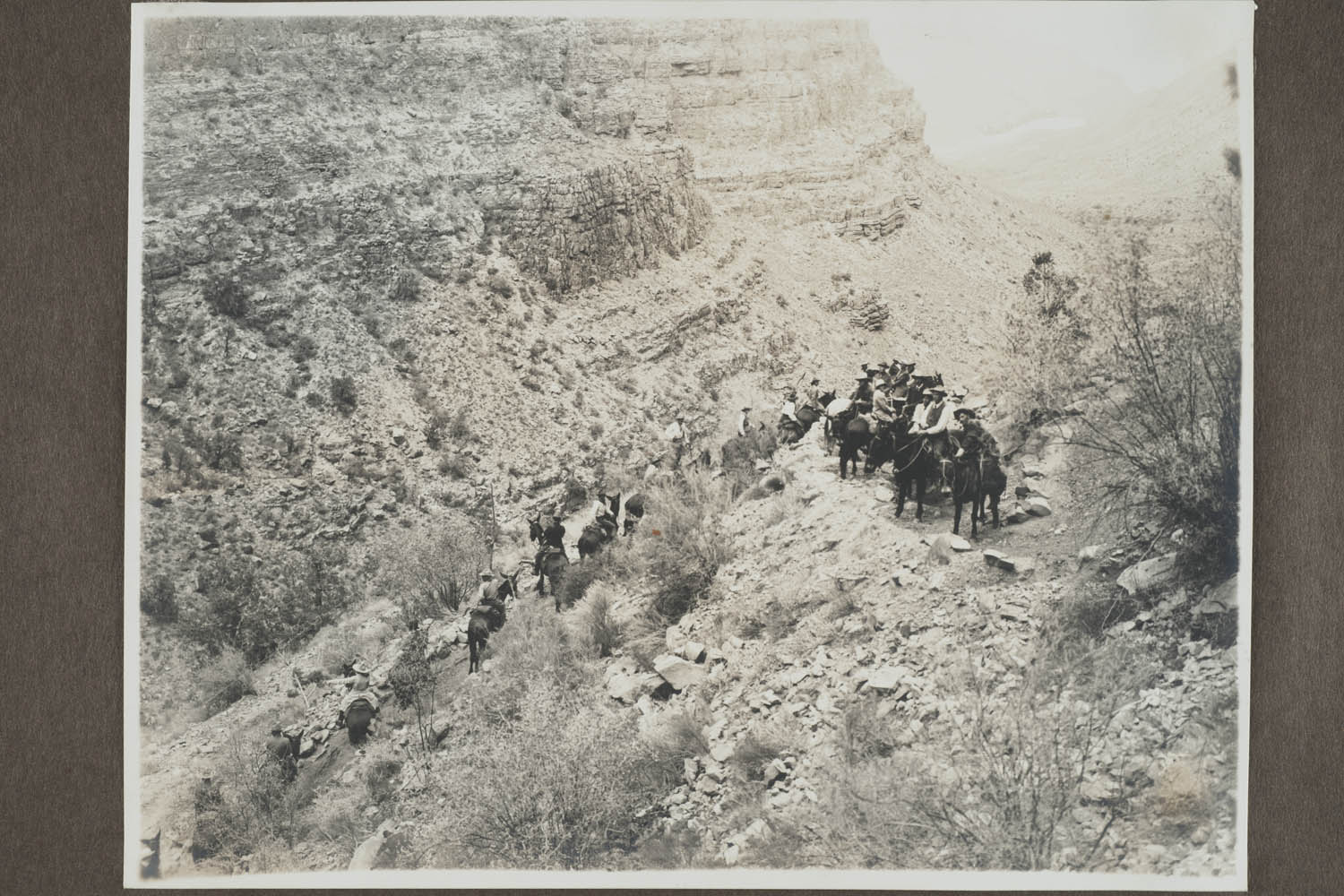 black & white photo of a group of people on horseback on rocking cliff trail