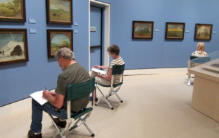 adults sitting in museum gallery sketching on paper