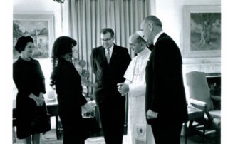 A group of men talking with a couple of women in a room