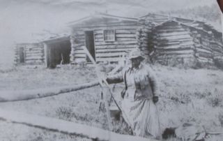 an African American woman standing in front of a log cabin building