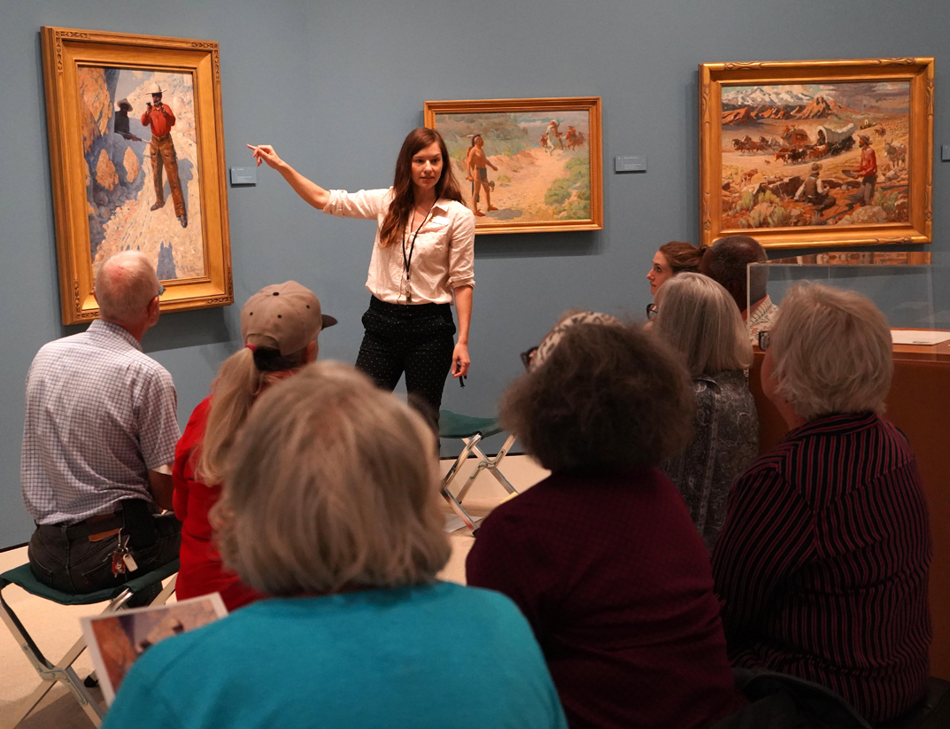 a woman standing in front of a group of people pointing to a painting