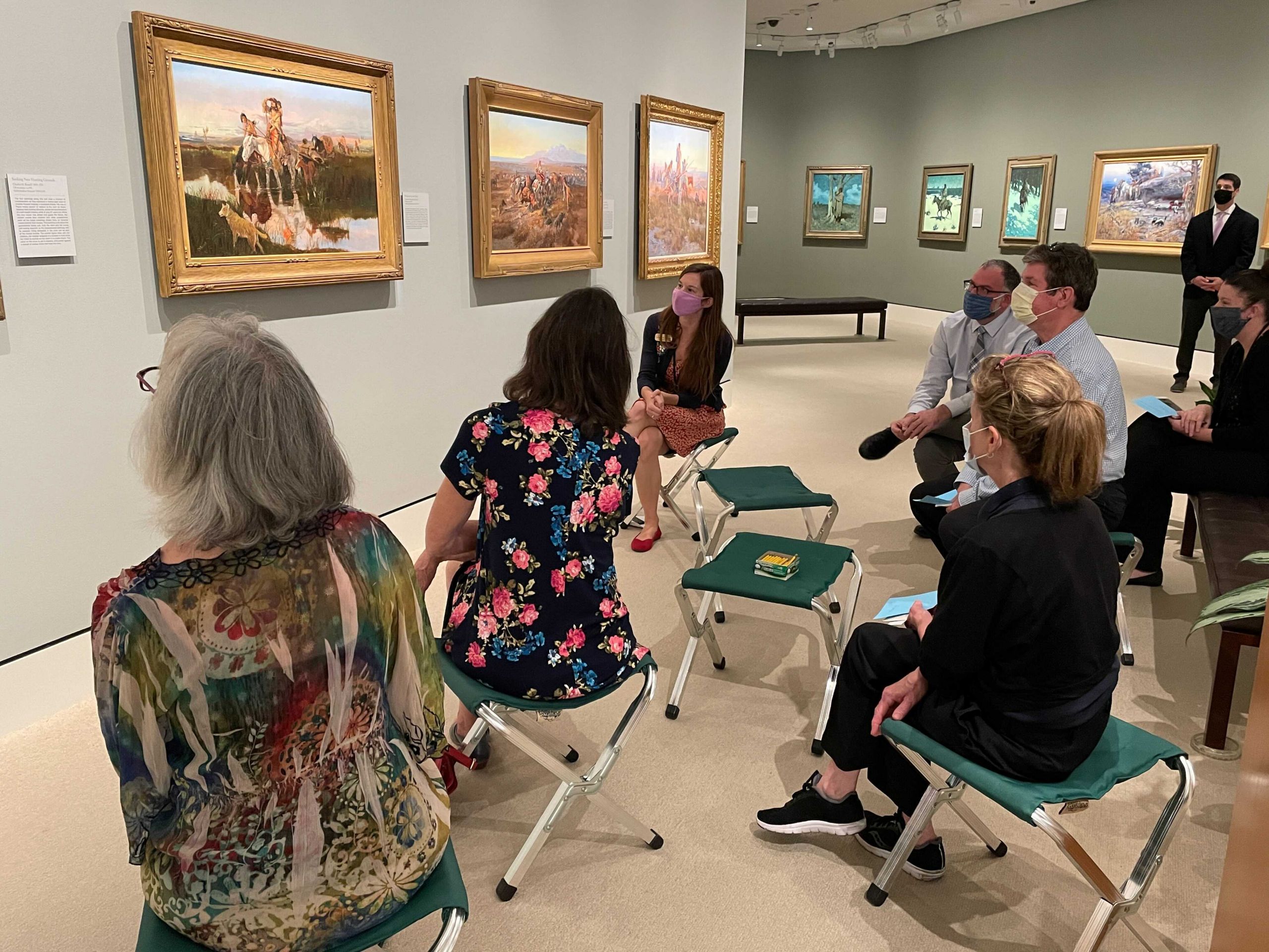 group of people sitting together in an art museum looking at a painting