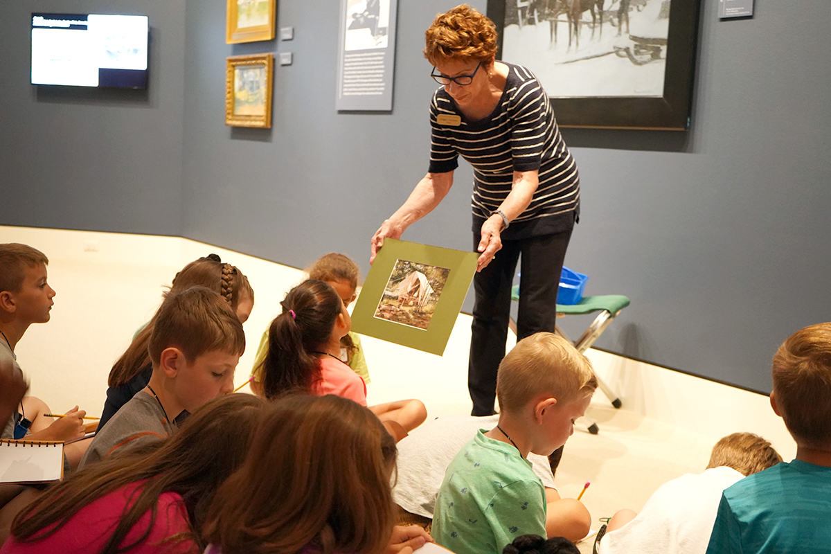woman sharing photo with children seated on floor in museum gallery