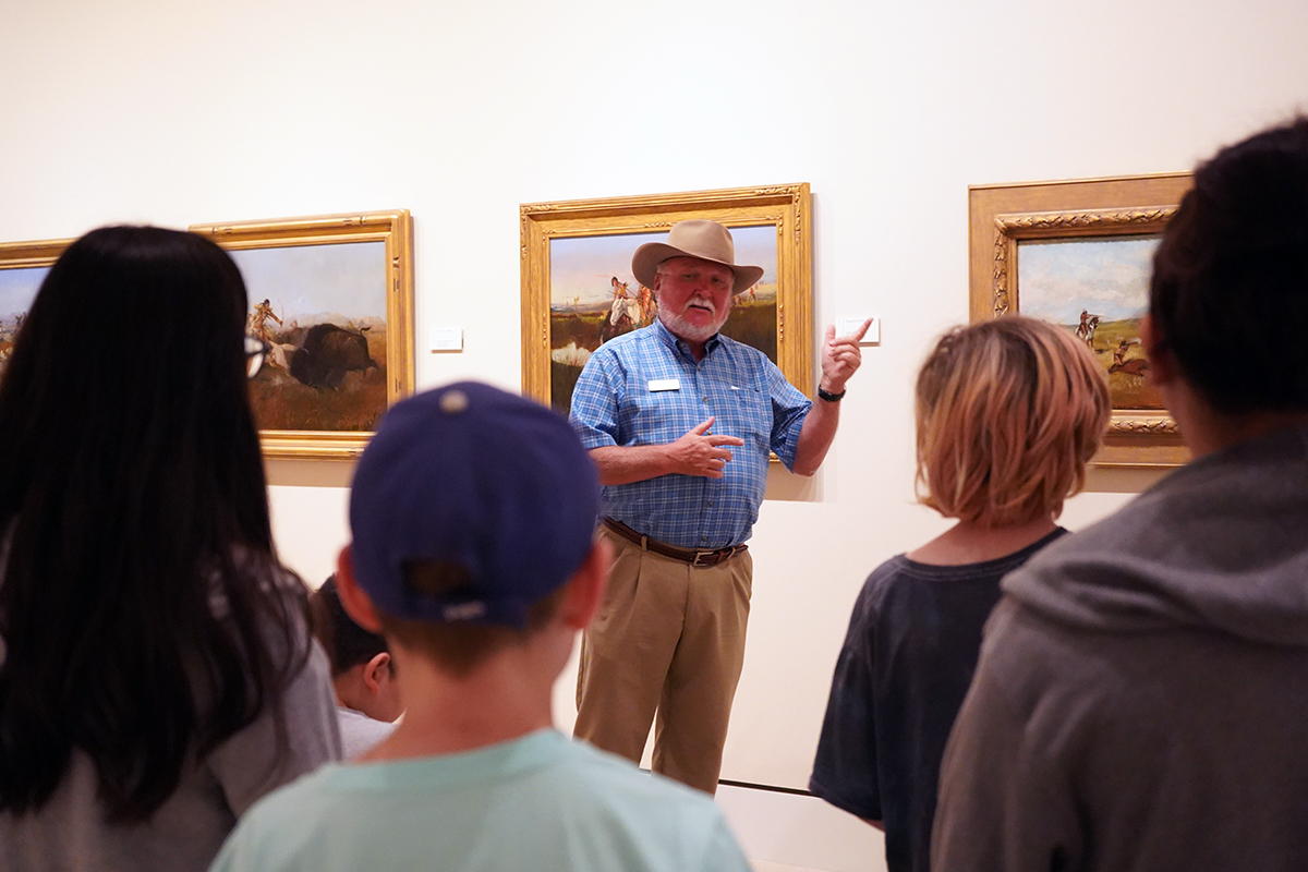 man in front of some paintings teaching to young adults in a museum gallery