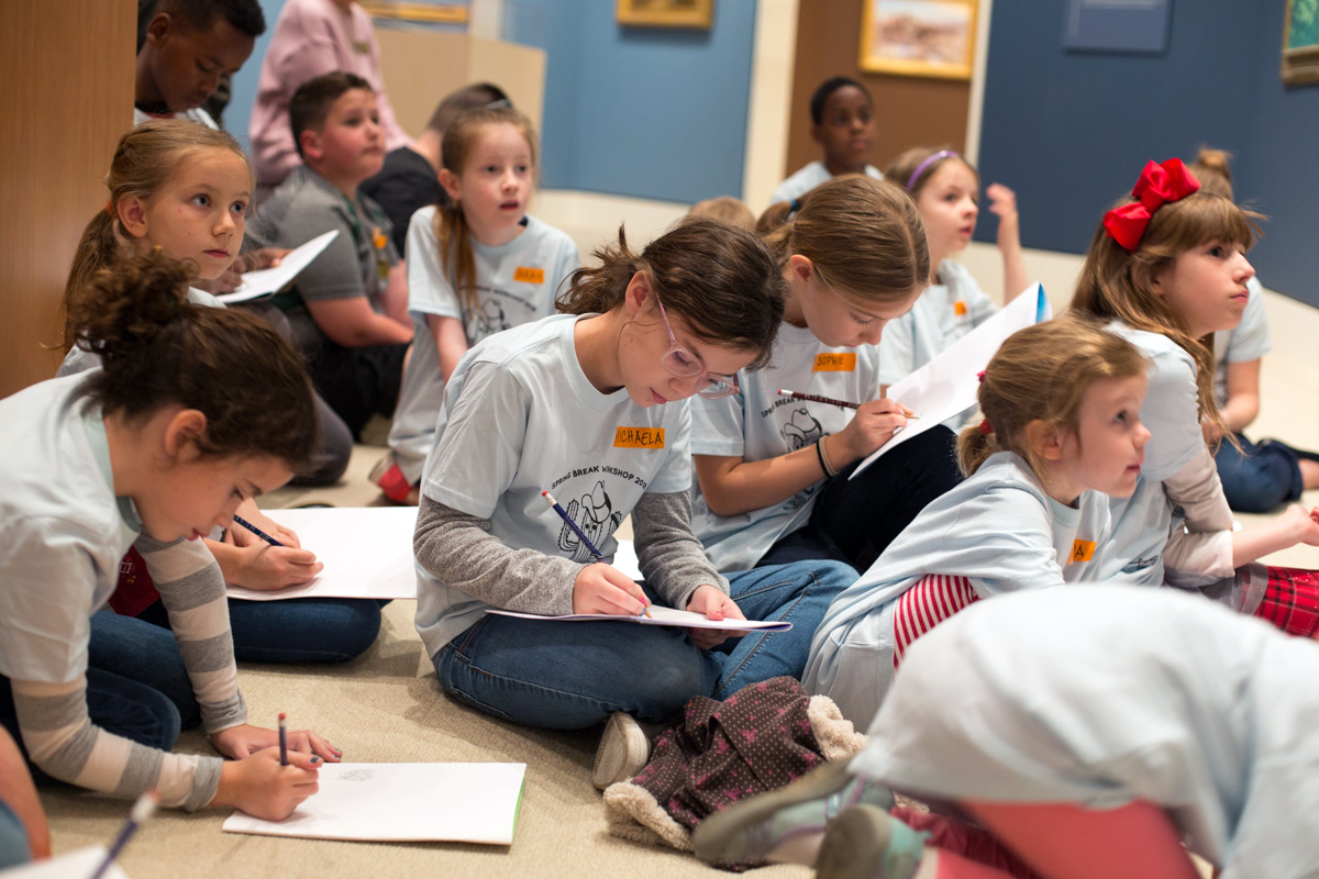 kids in camp t-shirts seated on ground drawing