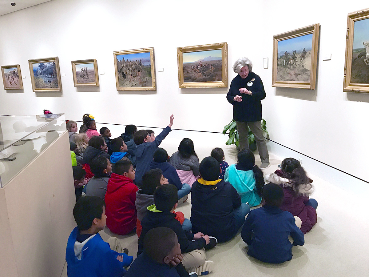 woman teaching to children seated on floor in art museum gallery