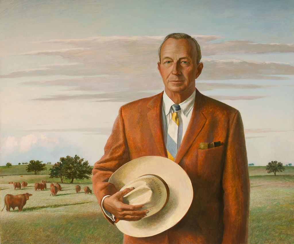A half-length portrait of a man in a suit, holding a cowboy hat.