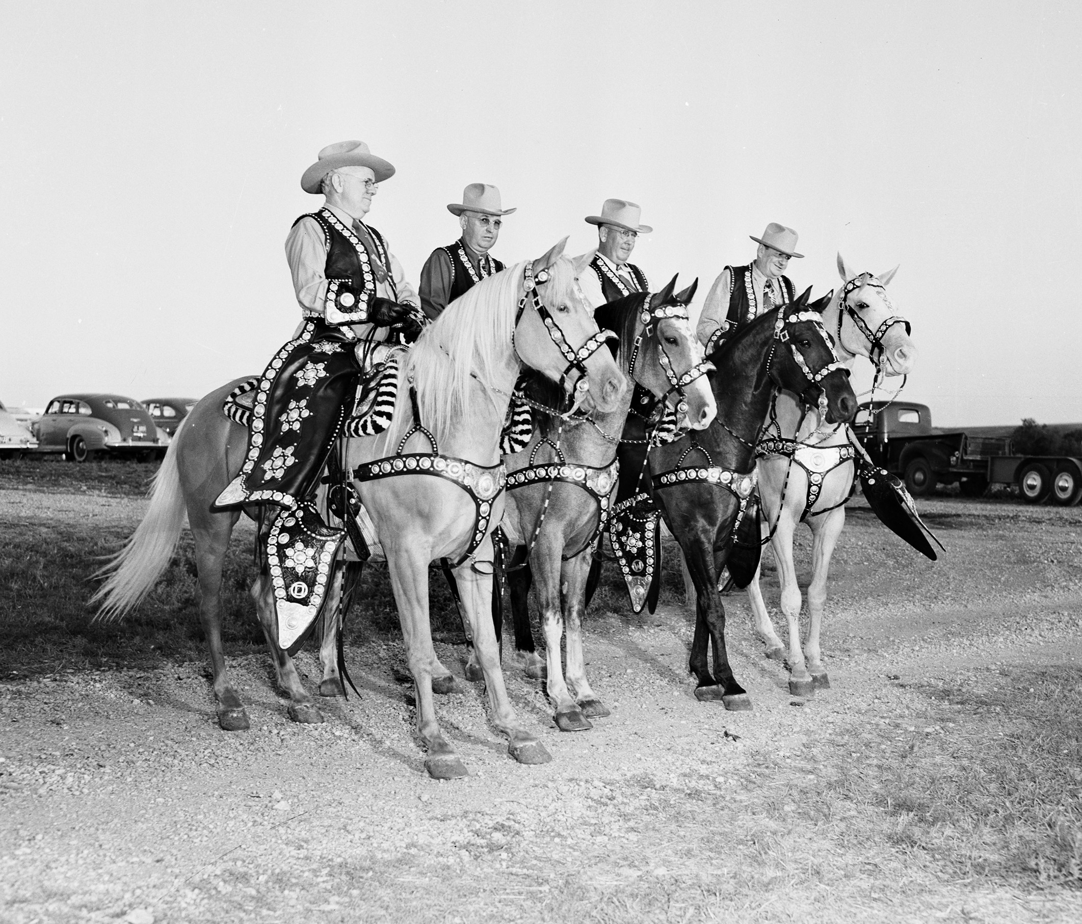 Four men in a row mounted on horses decked out in leather and silverwork parade gear