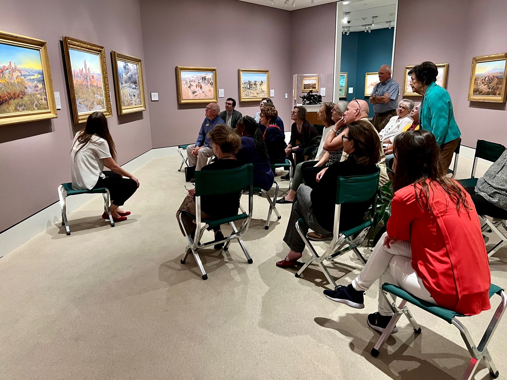 a group of people sitting in front of and looking at a painting
