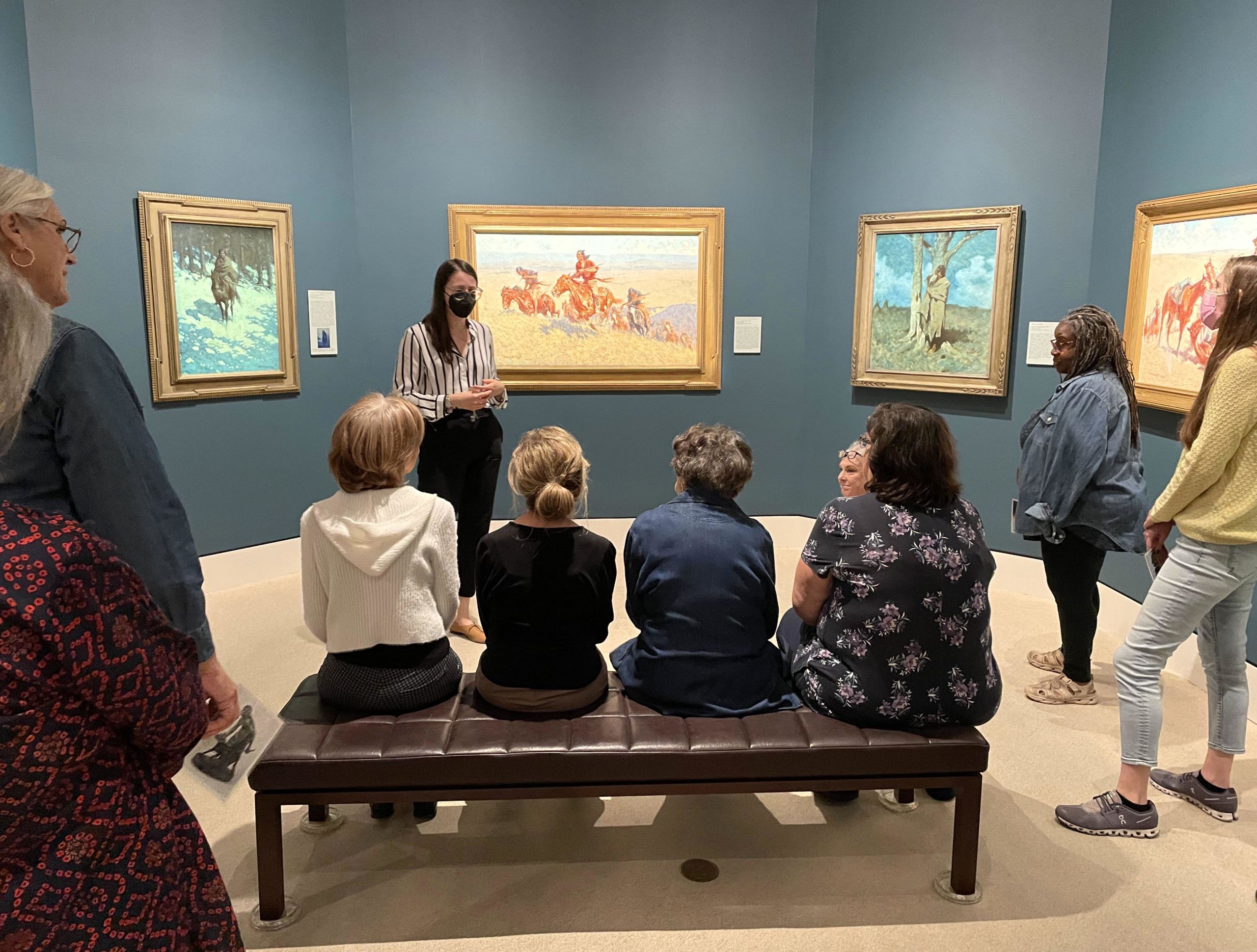 Adults sitting on a bench looking at art.