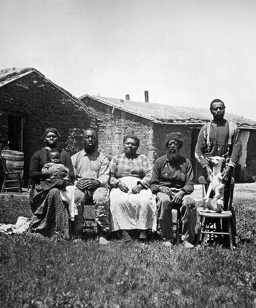A Black family sitting for a portrait in front of an old house.