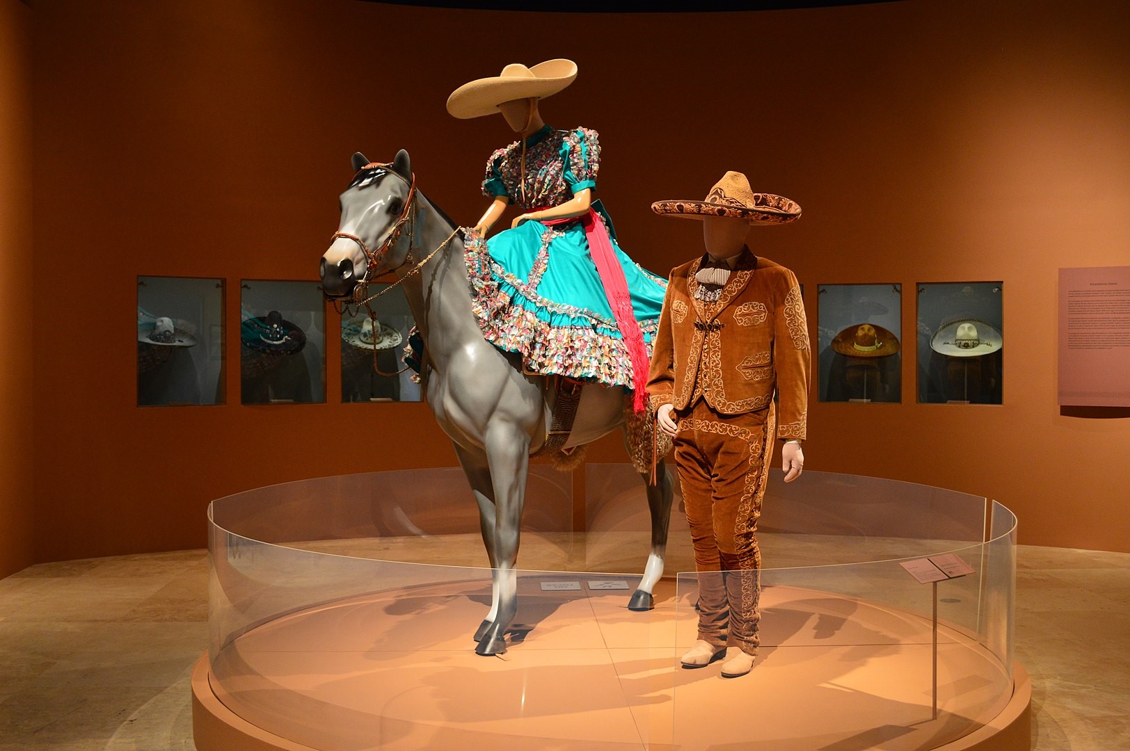 an installation of a mannequin dressed in male charro outfit standing next to mannequin on a horse dressed in female charro outfit