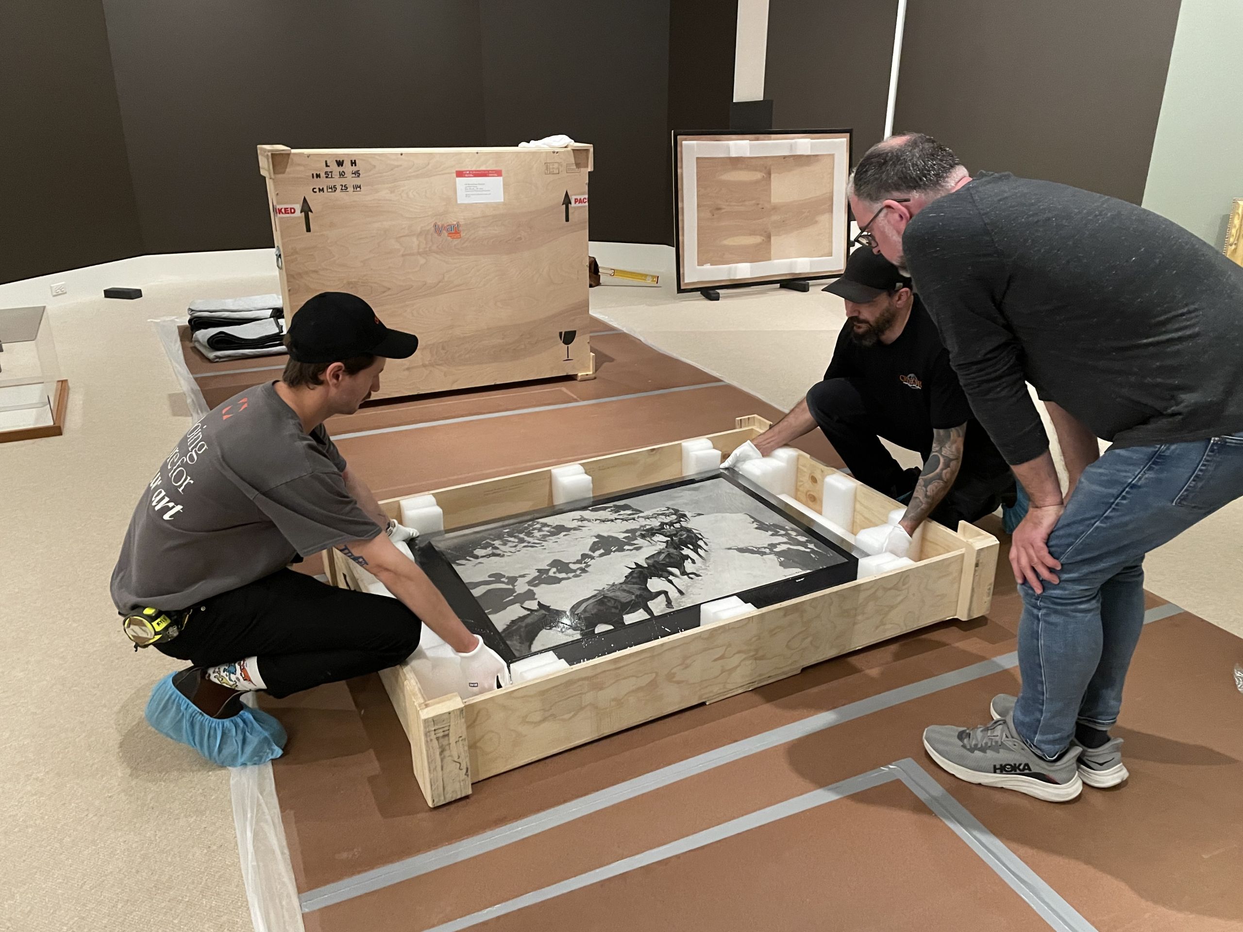 A group of guys lifting a painting out of a wooden crate.