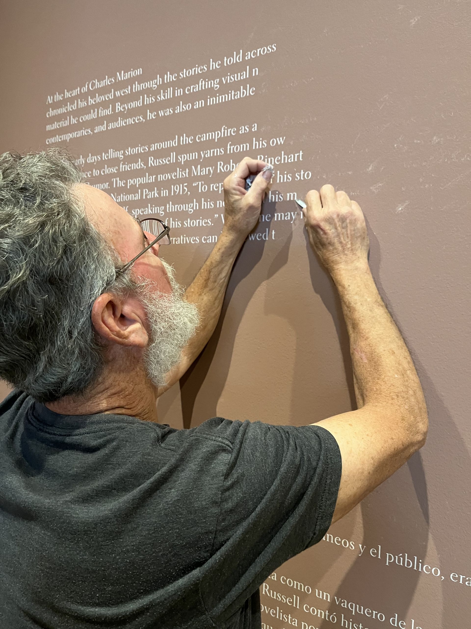 A man scraping off vinyl text from a wall.