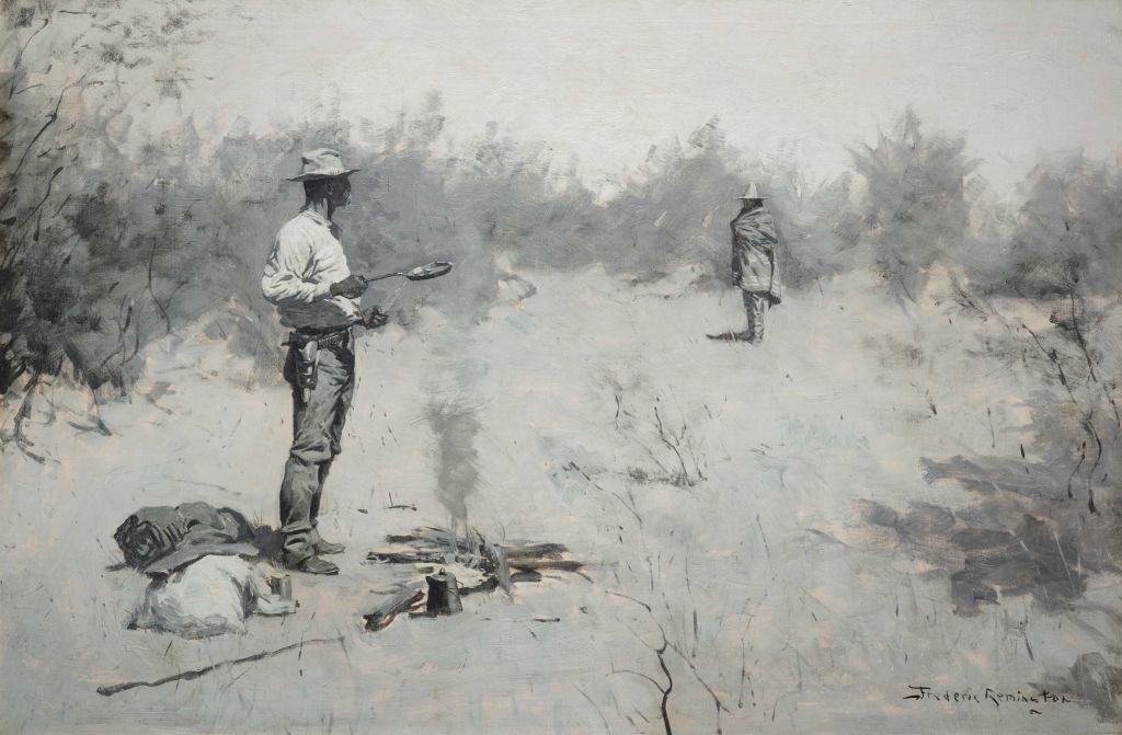 A man standing over a smoking campfire as another man approaches from the distance.