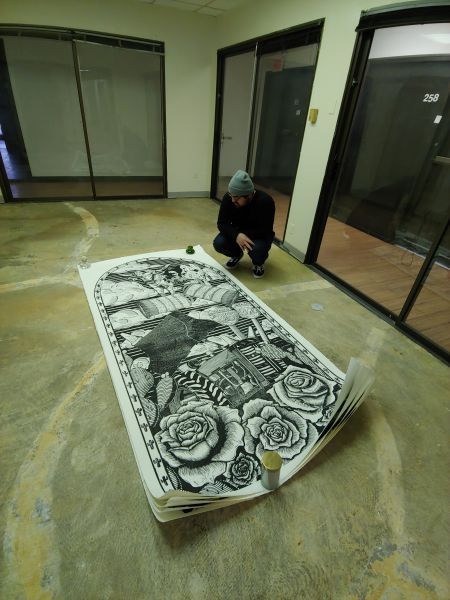 man kneeling next to large woodblock print on floor