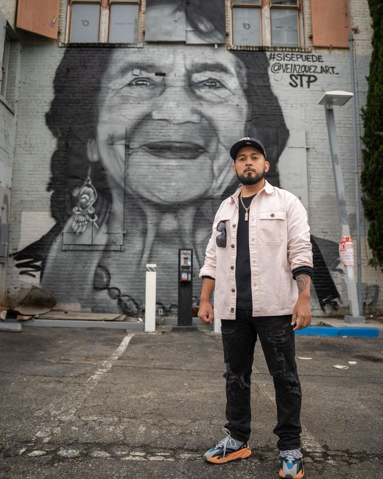 man standing in front of a mural of Dolores Huerta