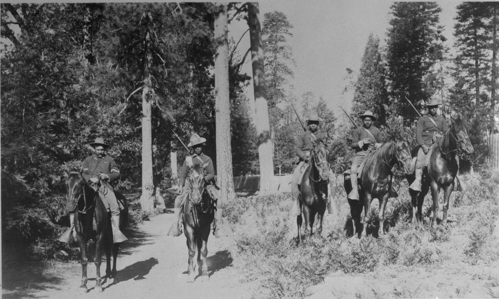 A group of mounted black soldiers in a forested background.