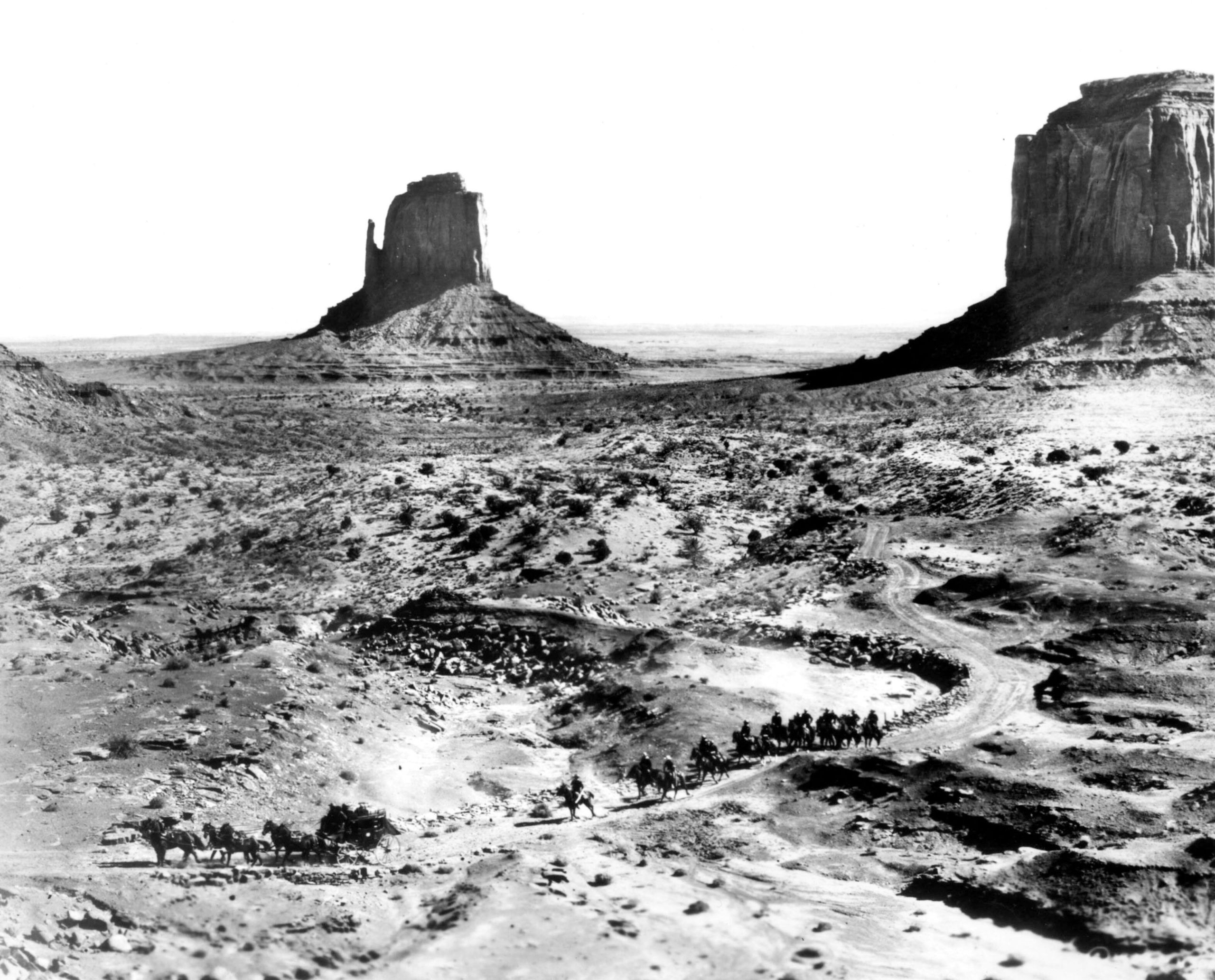 Distant shot of a stagecoach and caravan of horses traveling through the desert of Monument Valley