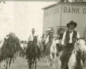 Group of men on horseback strolling down a town road