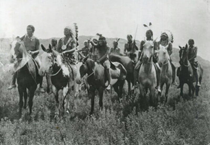 A large group of Native Americans in regalia in a field on horseback in