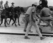 film director behind camera recording three men on horseback moving toward the camera