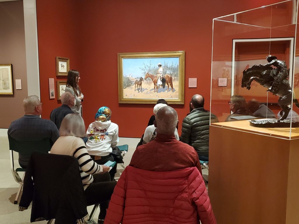 A group of people sitting in front of and talking about a painting in a museum gallery.