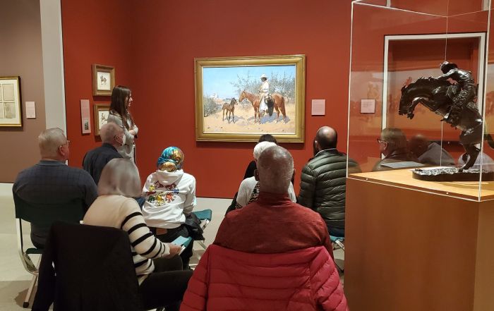 A group of people sitting in front of and talking about a painting in a museum gallery.