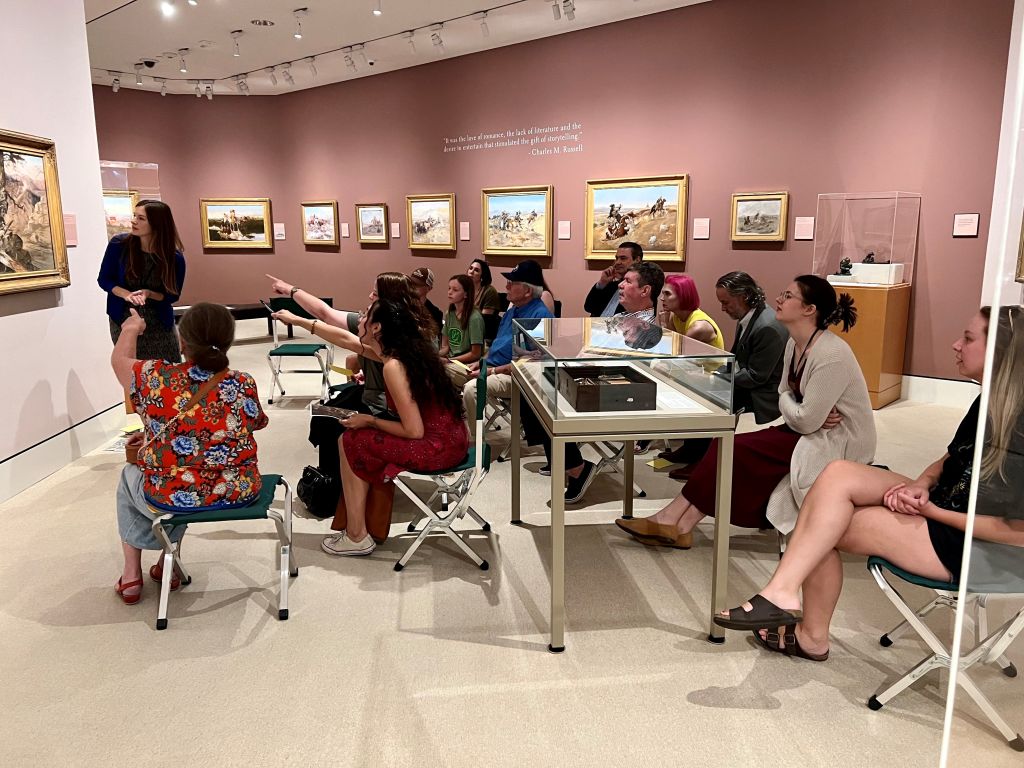 A group of people sitting in front of and looking at a work of art in a museum.